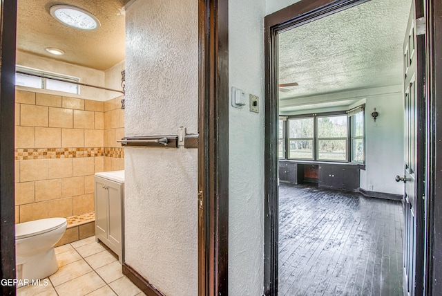 full bath featuring toilet, a textured ceiling, tile walls, tiled shower, and a textured wall