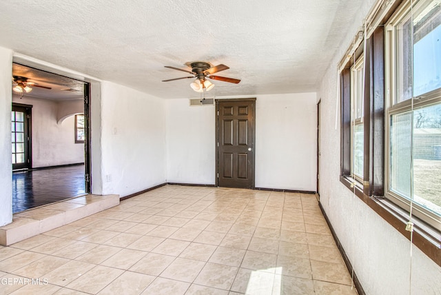 spare room with ceiling fan, light tile patterned floors, baseboards, and a textured ceiling