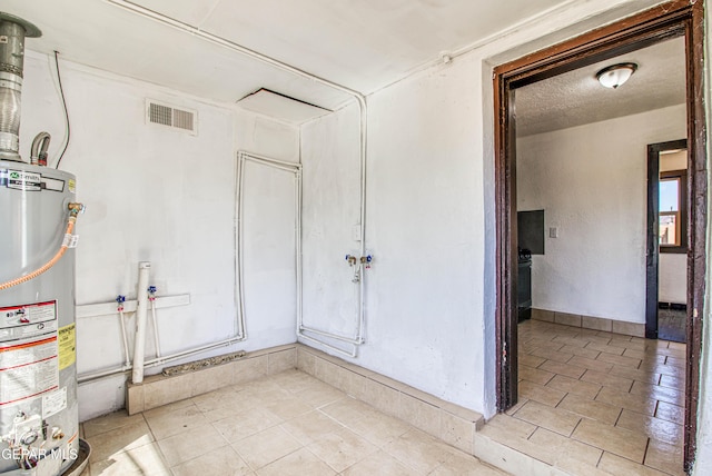 empty room with water heater, visible vents, a textured ceiling, and light tile patterned floors