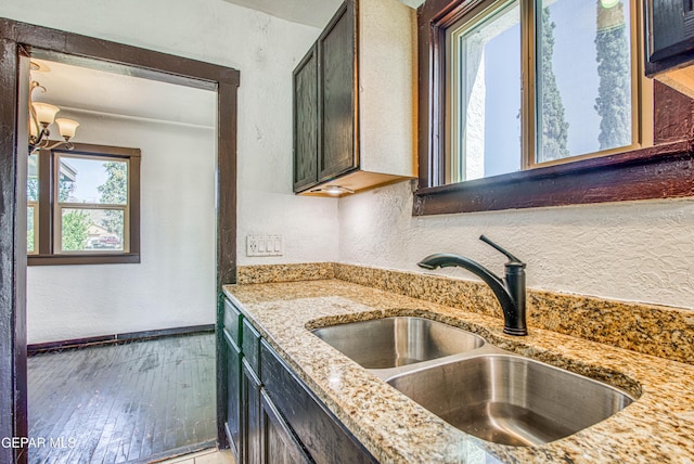 kitchen with light stone countertops, baseboards, a textured wall, and a sink