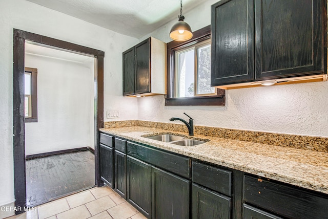 kitchen featuring light stone counters, light tile patterned floors, baseboards, a sink, and dark cabinets