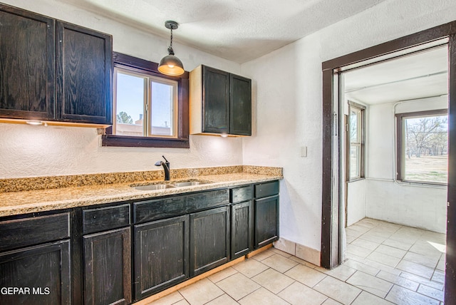 kitchen featuring light tile patterned floors, a sink, a textured ceiling, decorative light fixtures, and a textured wall