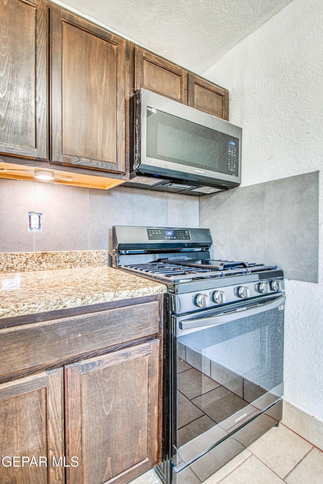 kitchen with a textured ceiling, backsplash, appliances with stainless steel finishes, light tile patterned flooring, and a textured wall