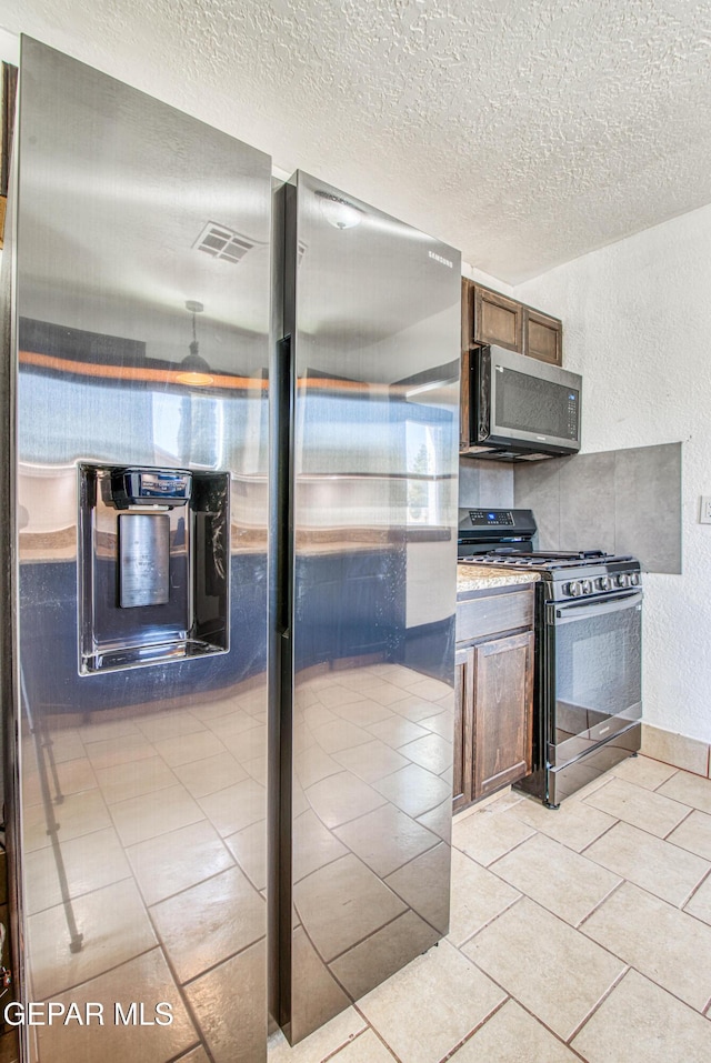 kitchen featuring light tile patterned floors, a textured ceiling, appliances with stainless steel finishes, and a textured wall