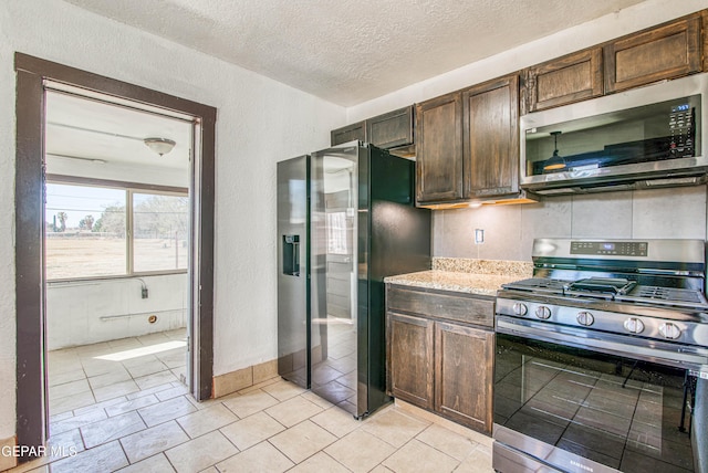 kitchen featuring a textured ceiling, appliances with stainless steel finishes, light tile patterned floors, dark brown cabinets, and a textured wall