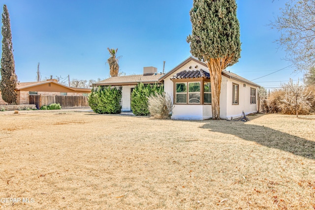 rear view of property featuring stucco siding, a lawn, and fence