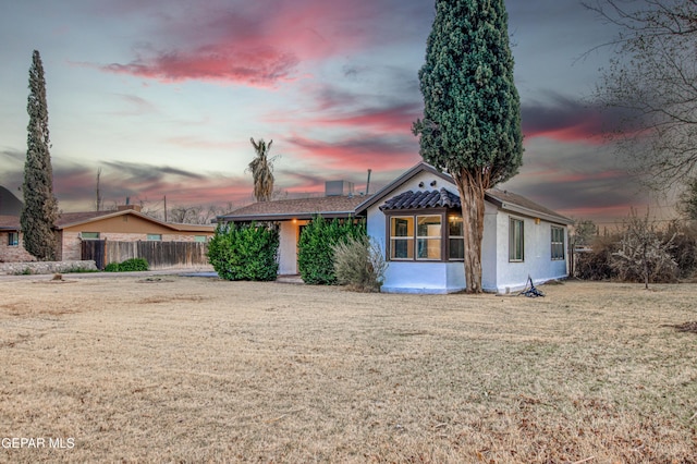 view of front of house featuring stucco siding, a lawn, and fence