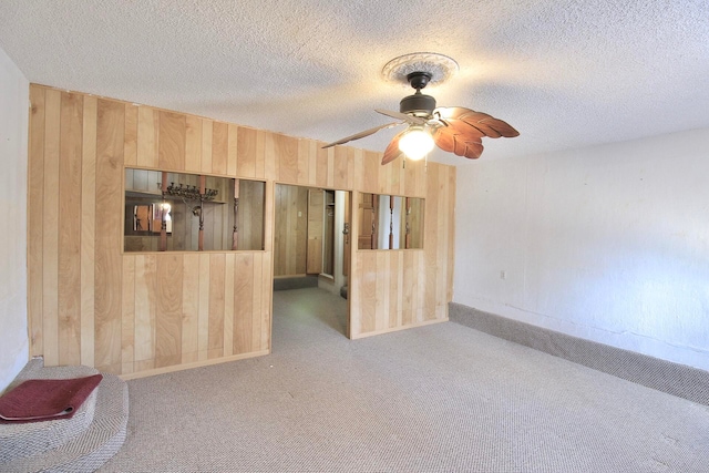 spare room with light carpet, a textured ceiling, ceiling fan, and wood walls