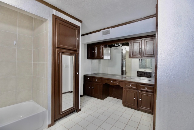 kitchen with light tile floors, crown molding, stainless steel counters, a textured ceiling, and dark brown cabinetry