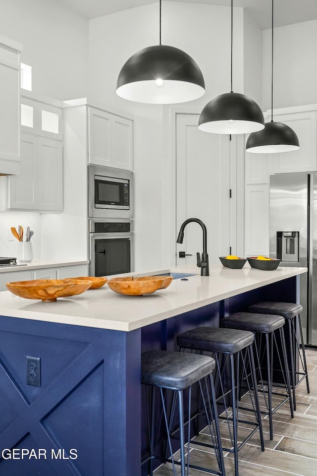 kitchen with white cabinetry, light countertops, appliances with stainless steel finishes, an island with sink, and pendant lighting