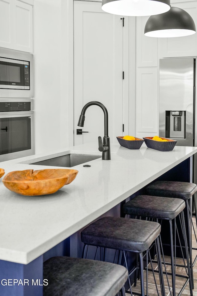 kitchen featuring stainless steel appliances, a breakfast bar area, a sink, and white cabinets