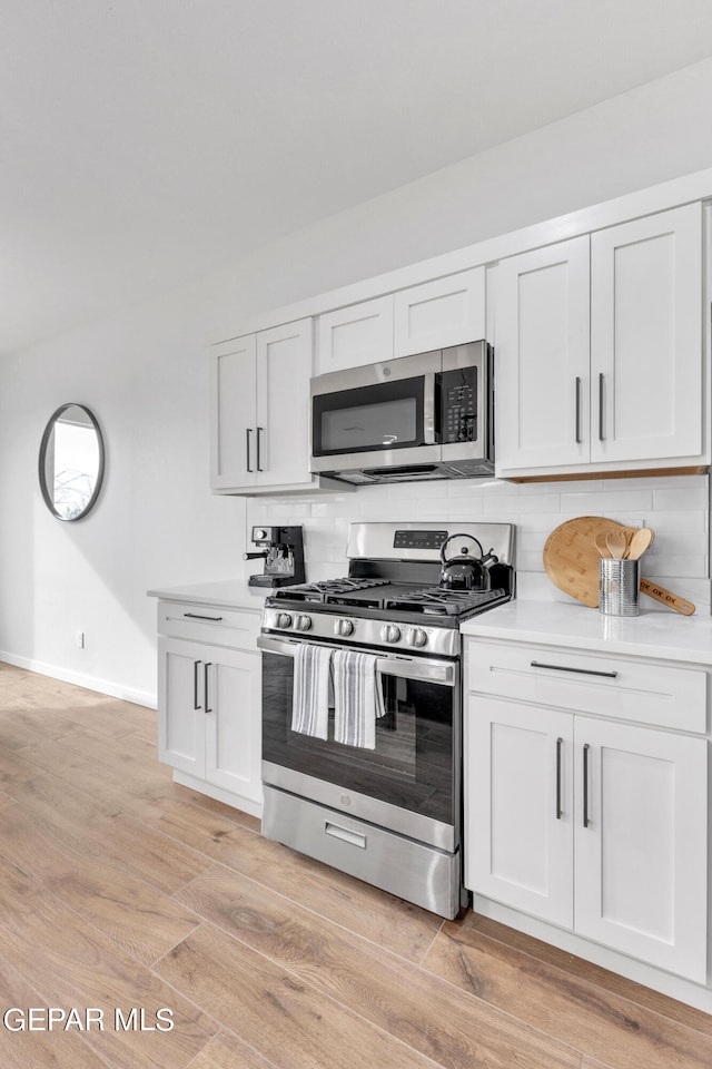 kitchen with white cabinets, backsplash, light hardwood / wood-style flooring, and appliances with stainless steel finishes