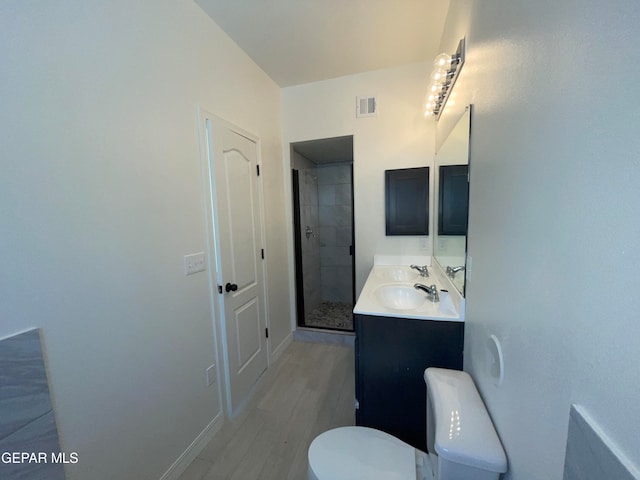 bathroom featuring toilet, tiled shower, vanity with extensive cabinet space, and hardwood / wood-style flooring