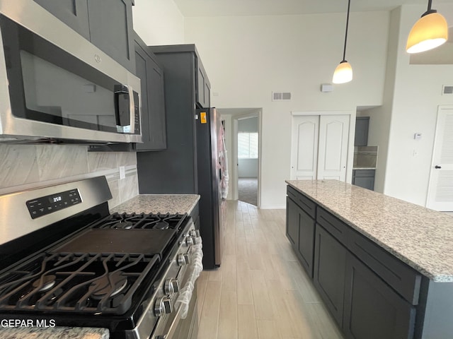 kitchen with light stone countertops, stainless steel appliances, light wood-type flooring, and decorative light fixtures