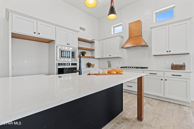 kitchen with pendant lighting, tasteful backsplash, white cabinets, custom range hood, and stainless steel microwave