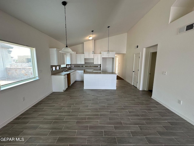 kitchen featuring white cabinetry, a kitchen island, dark tile patterned flooring, decorative light fixtures, and high vaulted ceiling