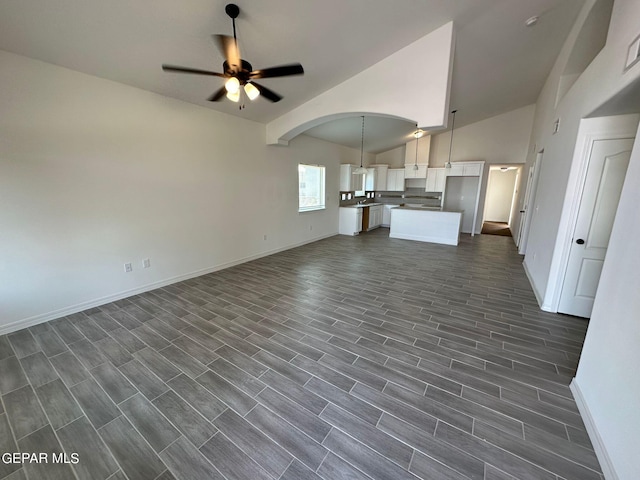 unfurnished living room featuring dark hardwood / wood-style floors, ceiling fan, and vaulted ceiling