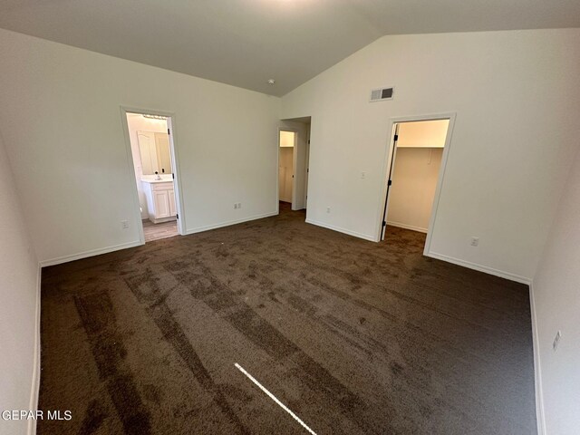 unfurnished bedroom featuring carpet floors, a spacious closet, vaulted ceiling, a closet, and ensuite bath