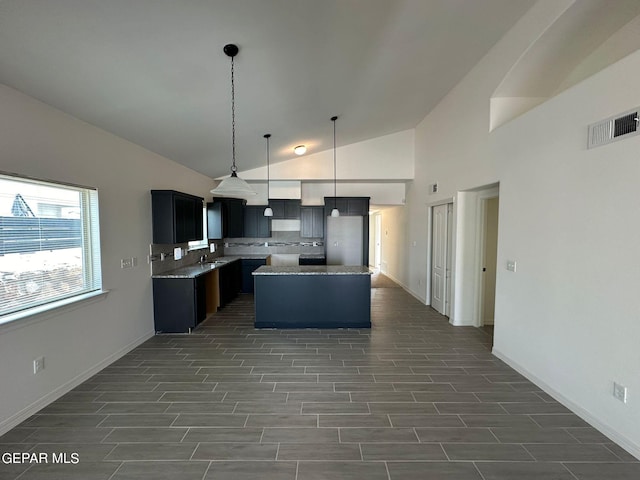 kitchen with tasteful backsplash, vaulted ceiling, sink, hanging light fixtures, and a center island