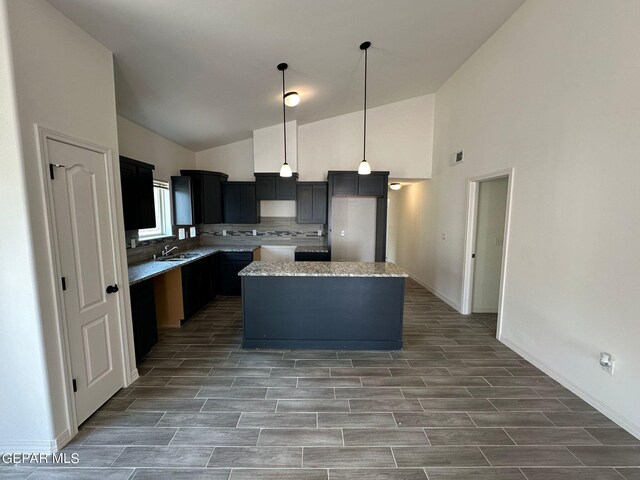 kitchen featuring hanging light fixtures, high vaulted ceiling, sink, a kitchen island, and backsplash