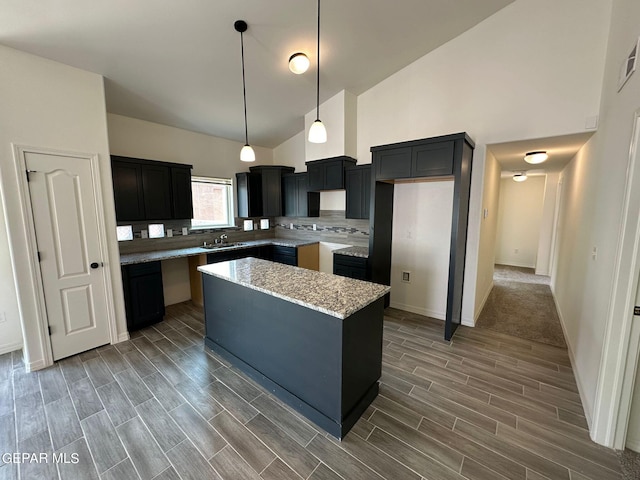 kitchen featuring light stone counters, hanging light fixtures, carpet flooring, a center island, and high vaulted ceiling