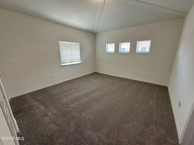 spare room featuring dark colored carpet and lofted ceiling