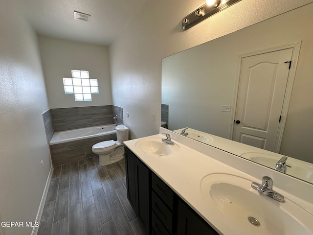 bathroom with double vanity, tiled tub, hardwood / wood-style floors, and toilet