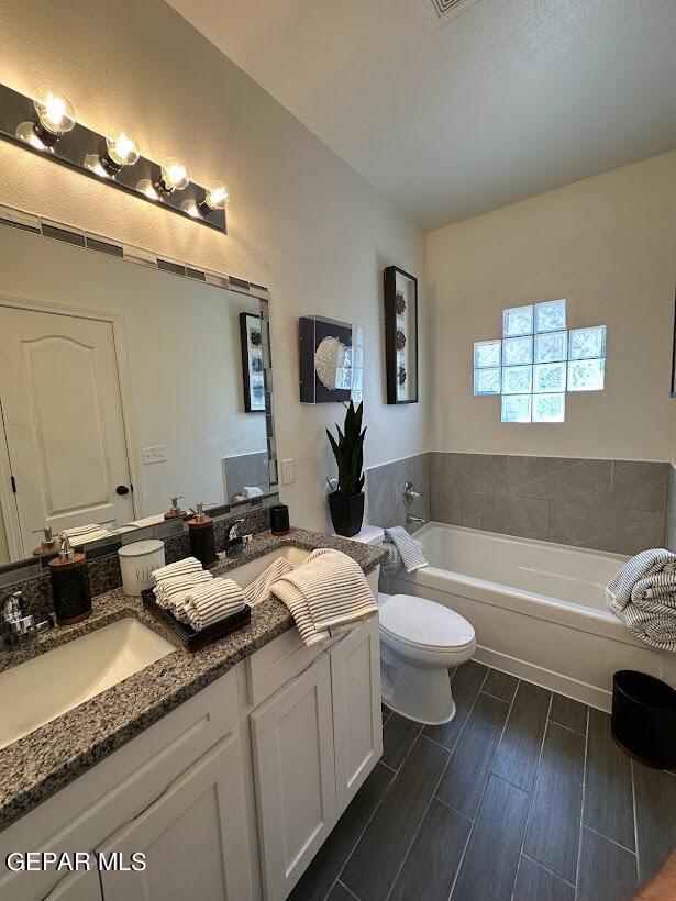 bathroom featuring double sink, a washtub, toilet, oversized vanity, and hardwood / wood-style flooring