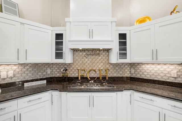 kitchen featuring custom exhaust hood, dark stone counters, stainless steel gas stovetop, tasteful backsplash, and white cabinets