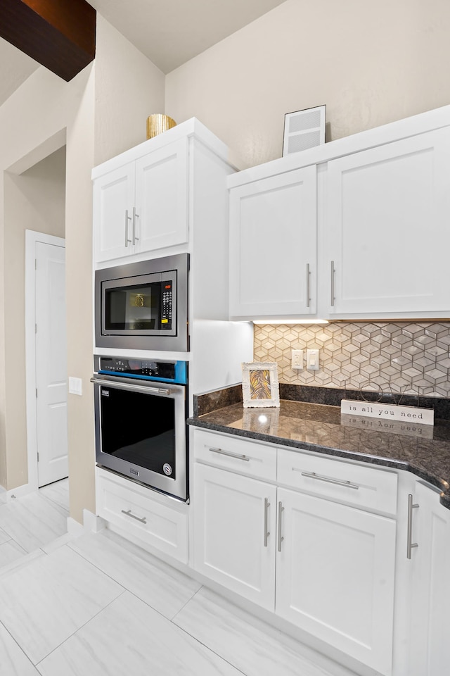 kitchen with dark stone countertops, white cabinets, backsplash, and stainless steel appliances