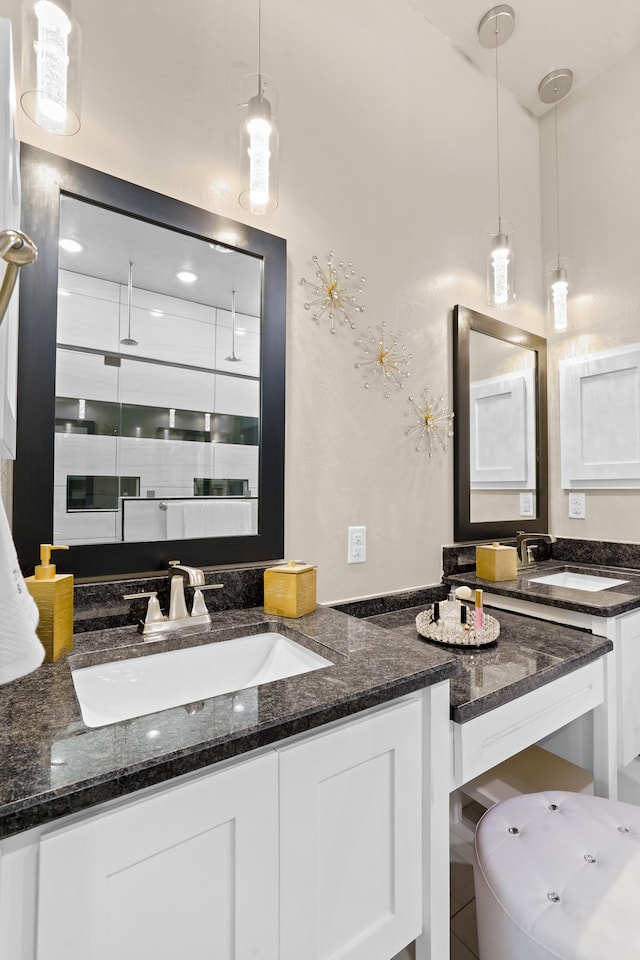 kitchen with white cabinetry, hanging light fixtures, dark stone countertops, and sink