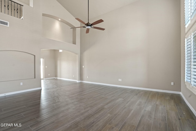 empty room with a healthy amount of sunlight, ceiling fan, high vaulted ceiling, and dark hardwood / wood-style floors