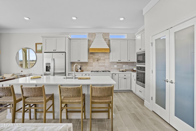 kitchen with white cabinets, a healthy amount of sunlight, custom range hood, and appliances with stainless steel finishes