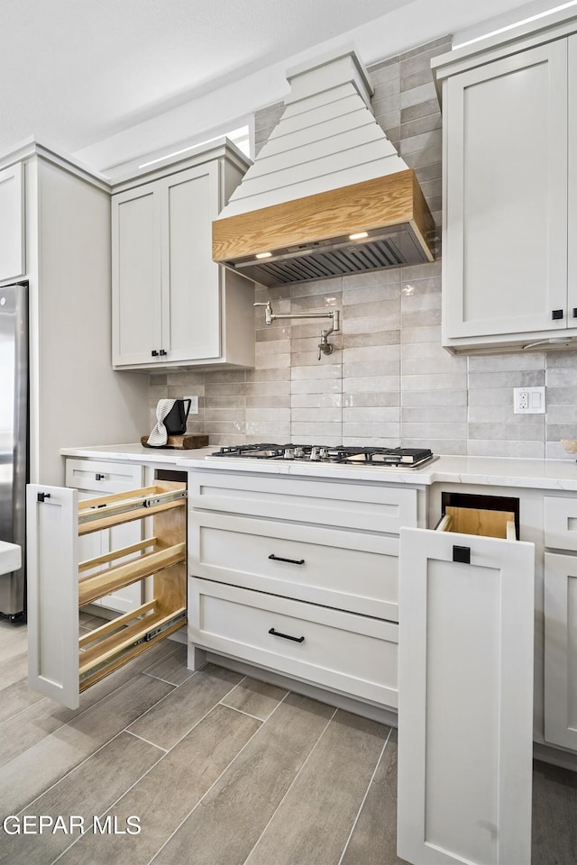 kitchen with decorative backsplash, light wood-type flooring, white gas cooktop, and custom exhaust hood