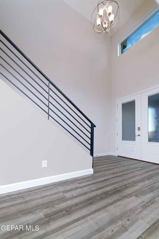 foyer entrance featuring a towering ceiling, hardwood / wood-style floors, an inviting chandelier, and french doors