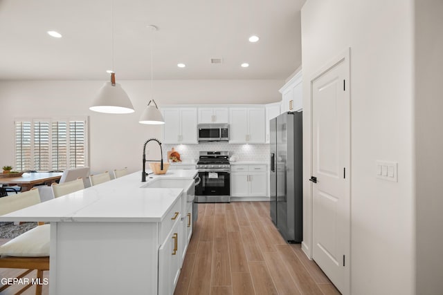 kitchen with white cabinets, a center island with sink, hanging light fixtures, appliances with stainless steel finishes, and tasteful backsplash