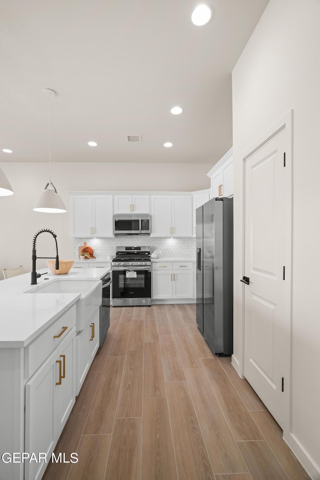 kitchen with white cabinets, decorative light fixtures, sink, and appliances with stainless steel finishes