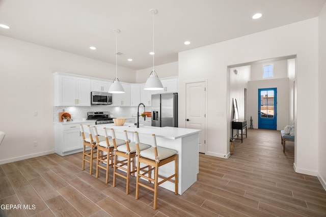 kitchen with a center island with sink, a kitchen breakfast bar, hanging light fixtures, white cabinetry, and stainless steel appliances