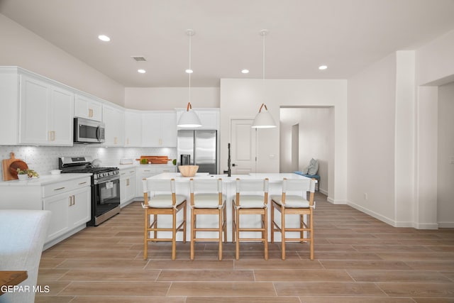 kitchen featuring decorative backsplash, appliances with stainless steel finishes, pendant lighting, a center island with sink, and white cabinetry