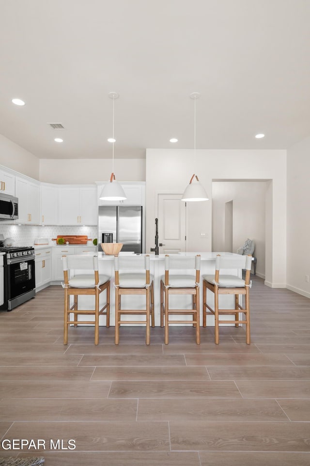 kitchen with pendant lighting, white cabinetry, stainless steel appliances, and a kitchen island with sink