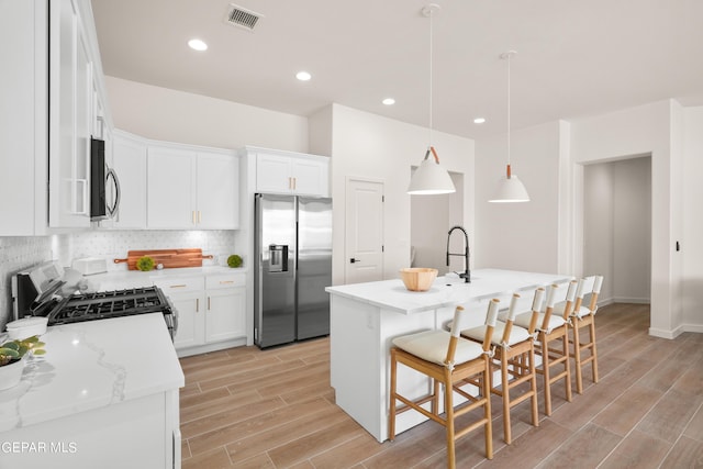 kitchen featuring white cabinetry, an island with sink, stainless steel appliances, and decorative light fixtures