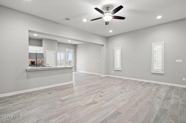 unfurnished living room featuring ceiling fan, sink, and light wood-type flooring