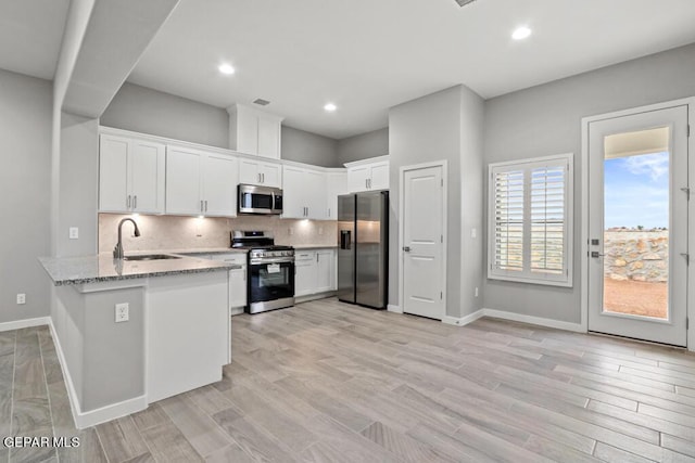 kitchen with light stone countertops, kitchen peninsula, stainless steel appliances, light hardwood / wood-style floors, and white cabinetry