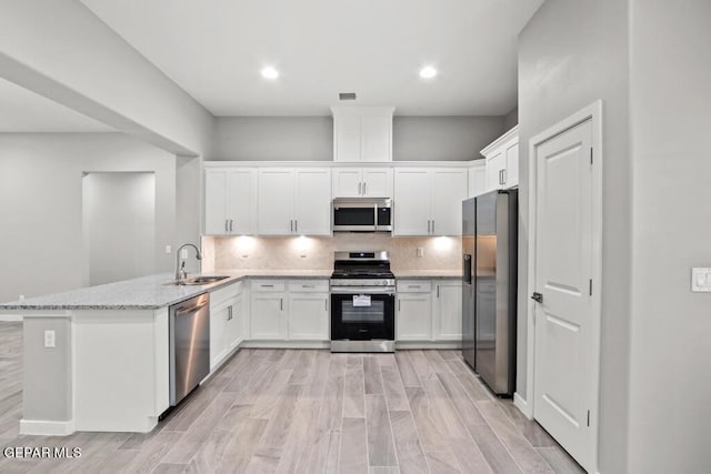 kitchen featuring kitchen peninsula, light stone countertops, stainless steel appliances, sink, and white cabinetry