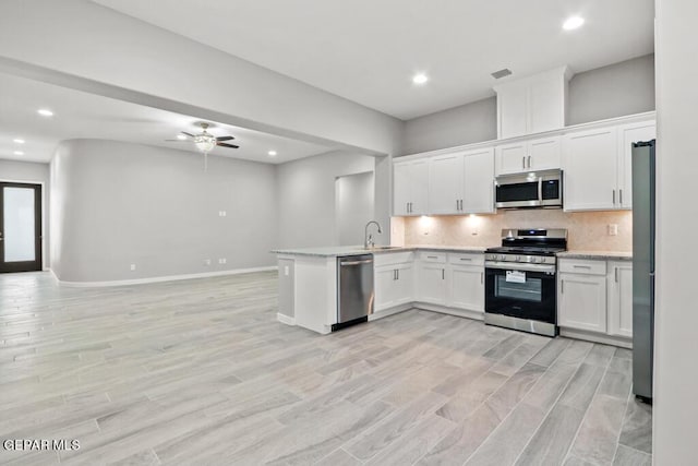 kitchen featuring sink, stainless steel appliances, light hardwood / wood-style flooring, kitchen peninsula, and white cabinets