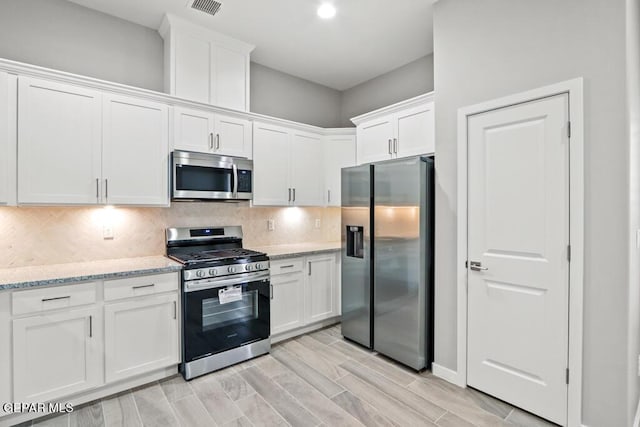 kitchen featuring white cabinets, appliances with stainless steel finishes, backsplash, and light stone counters