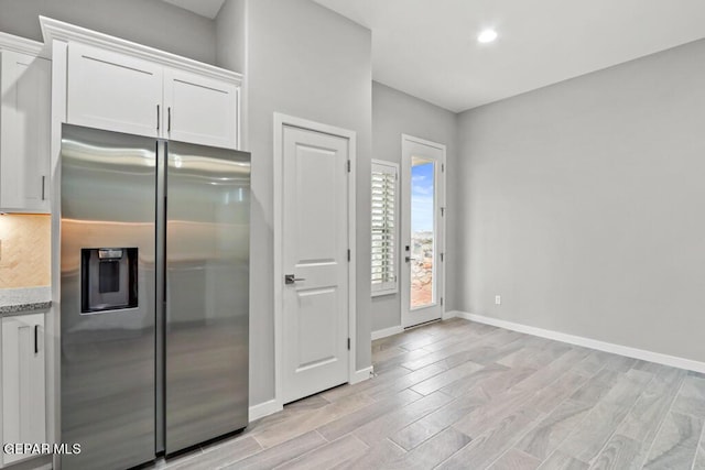 kitchen with white cabinetry, stainless steel fridge with ice dispenser, light hardwood / wood-style floors, and light stone counters