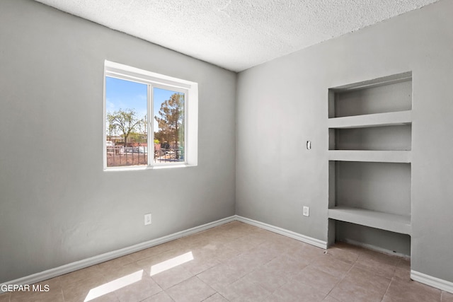 tiled empty room with a textured ceiling and built in shelves