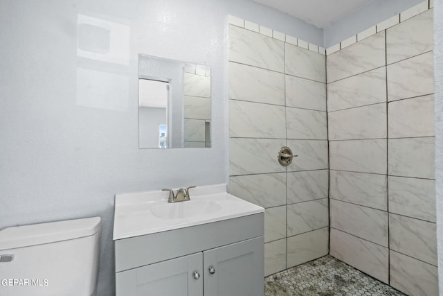 bathroom featuring tiled shower, toilet, and large vanity