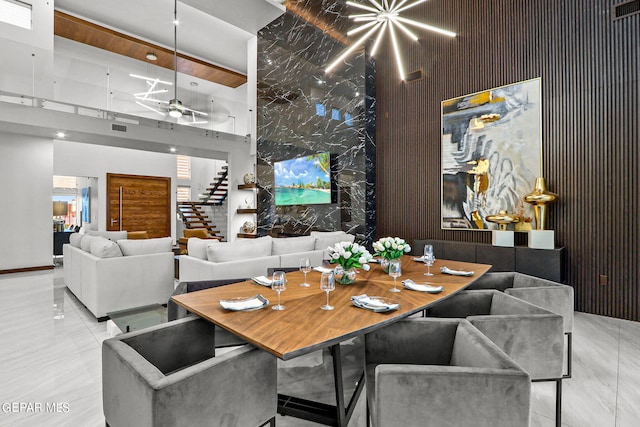 dining area with a towering ceiling, light tile floors, and ceiling fan with notable chandelier